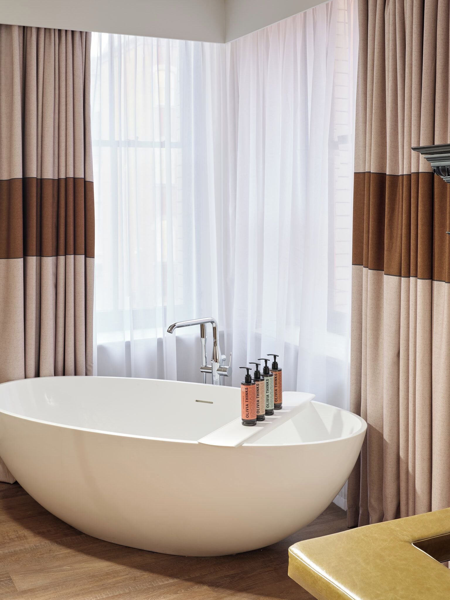 A modern bathroom with a freestanding bathtub, a faucet, and toiletries on the edge.