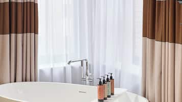 A modern bathroom with a freestanding bathtub, a faucet, and toiletries on the edge.