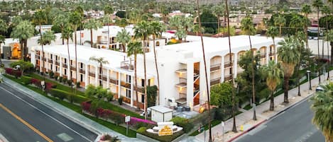 A hotel with multiple floors, palm trees, and a mountainous backdrop.