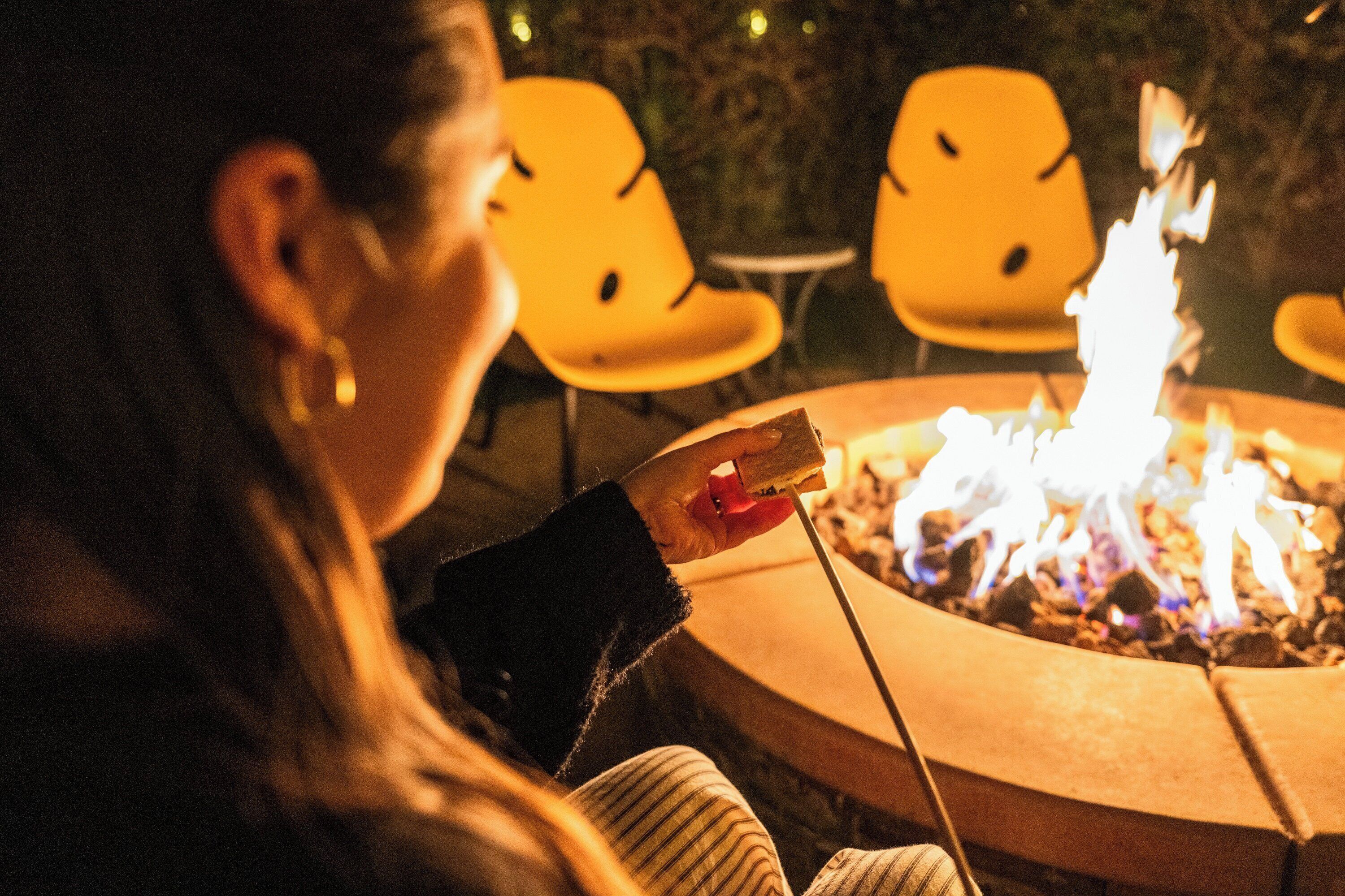 A person sitting by a circular fire pit with chairs around it.