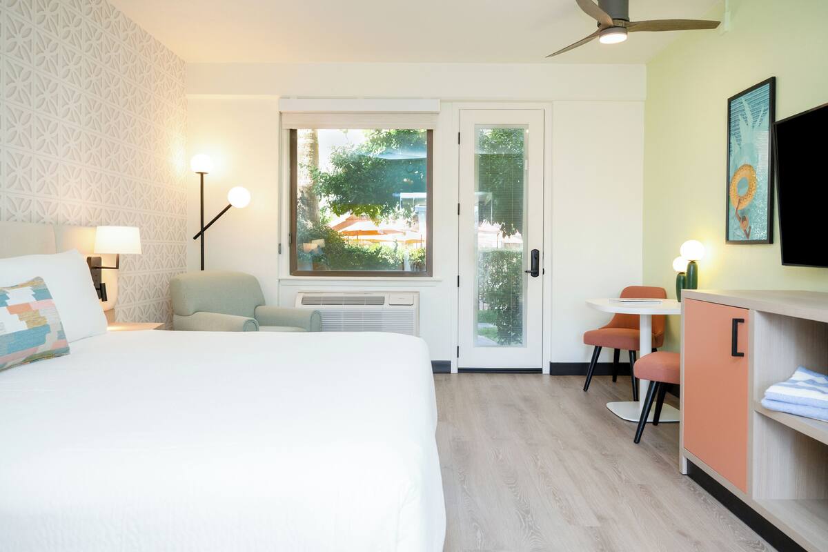 A hotel room with a bed, a desk, a chair, a TV, and a window with a view of the outdoors.