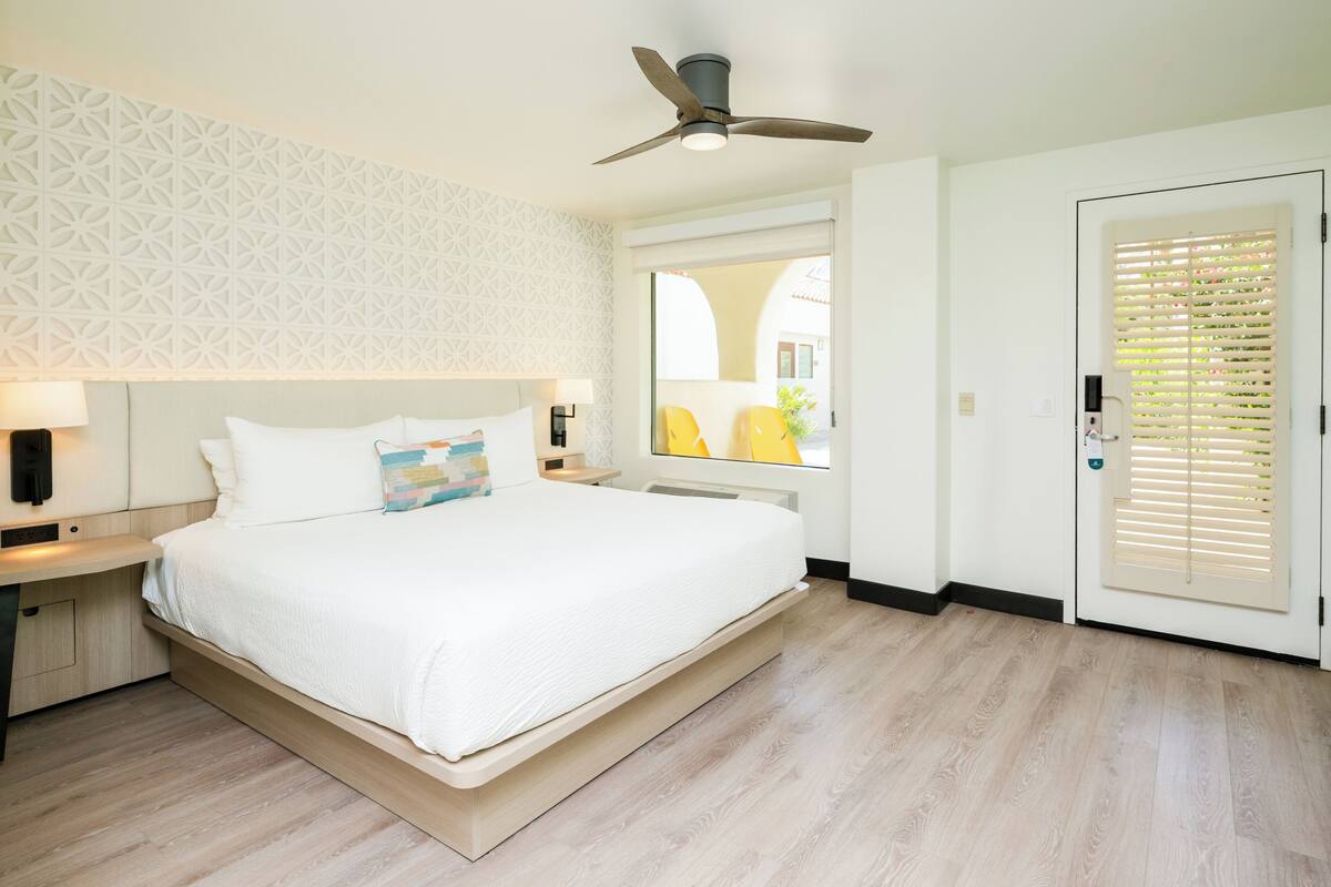 A modern bedroom with a bed, bedside tables, a ceiling fan, and a window with blinds.