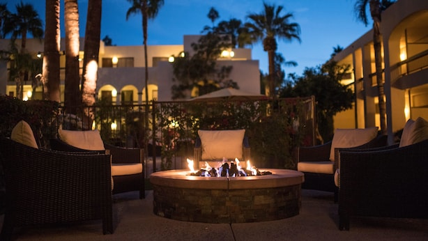 A circular fire pit with seating, surrounded by palm trees and a building in the background. - Palm Mountain Resort and Spa (Palm Springs)