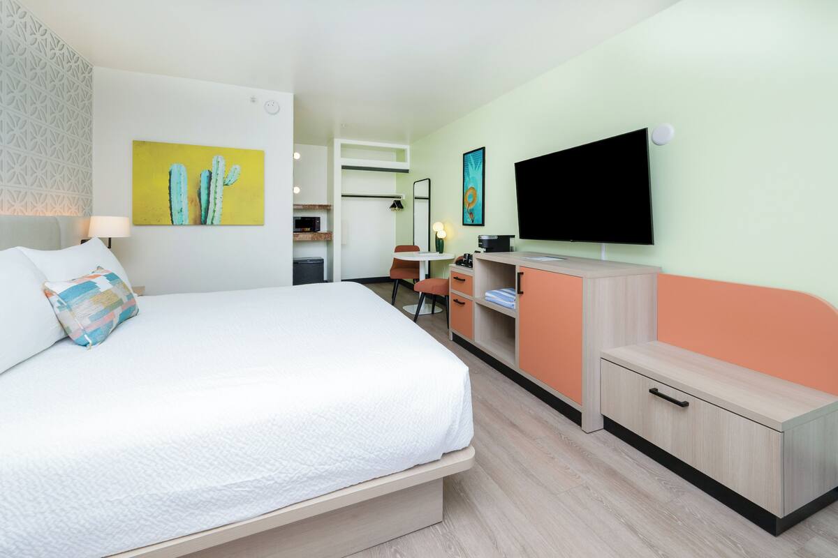 A hotel room with a bed, a desk, a television, and artwork on the walls.