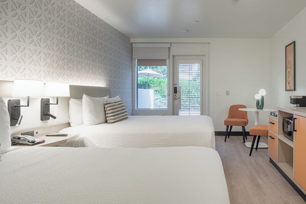 A hotel room with two beds, a desk, a chair, a TV, and a window with blinds.