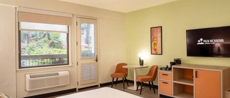 Une chambre d’hôtel comprenant un lit, un bureau avec deux chaises, une télévision et une grande fenêtre avec des stores.