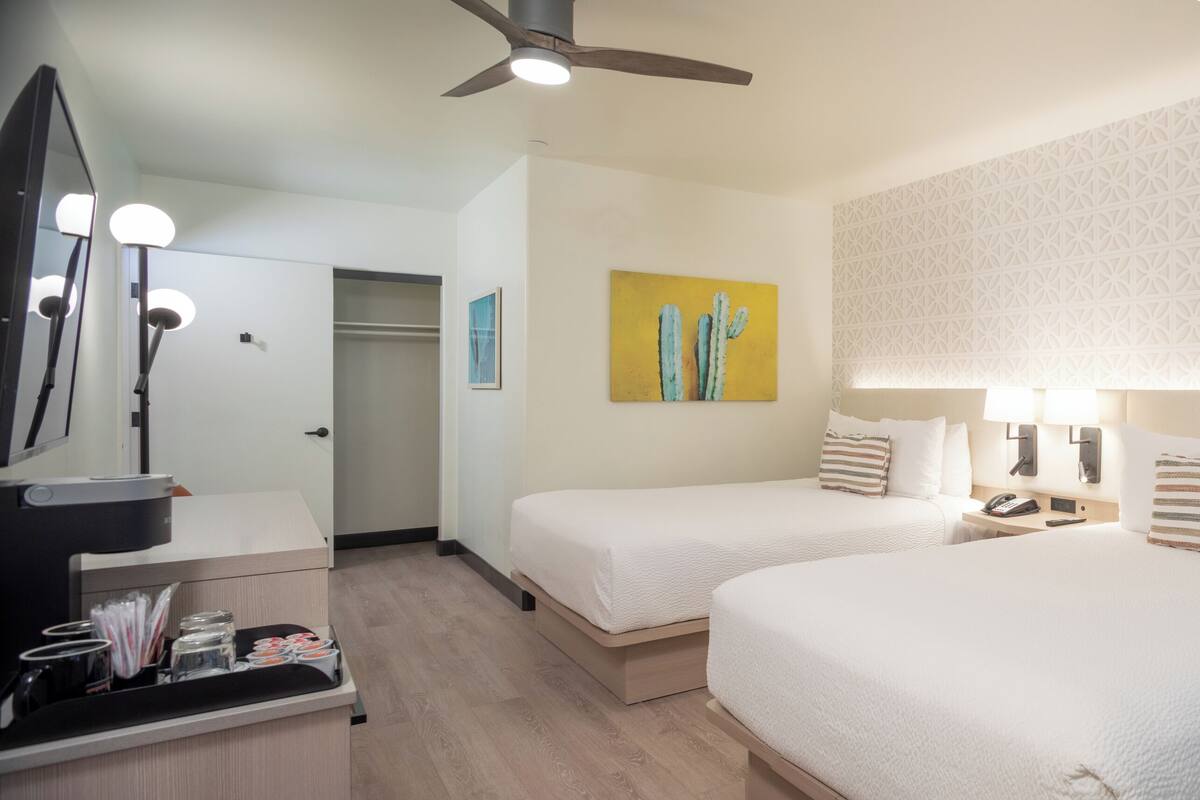 A hotel room with two beds, a vanity with a mirror, and a wall with a geometric pattern.