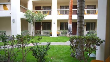 Un hotel de varios pisos con balcones, un patio central con césped y árboles, y una palmera.