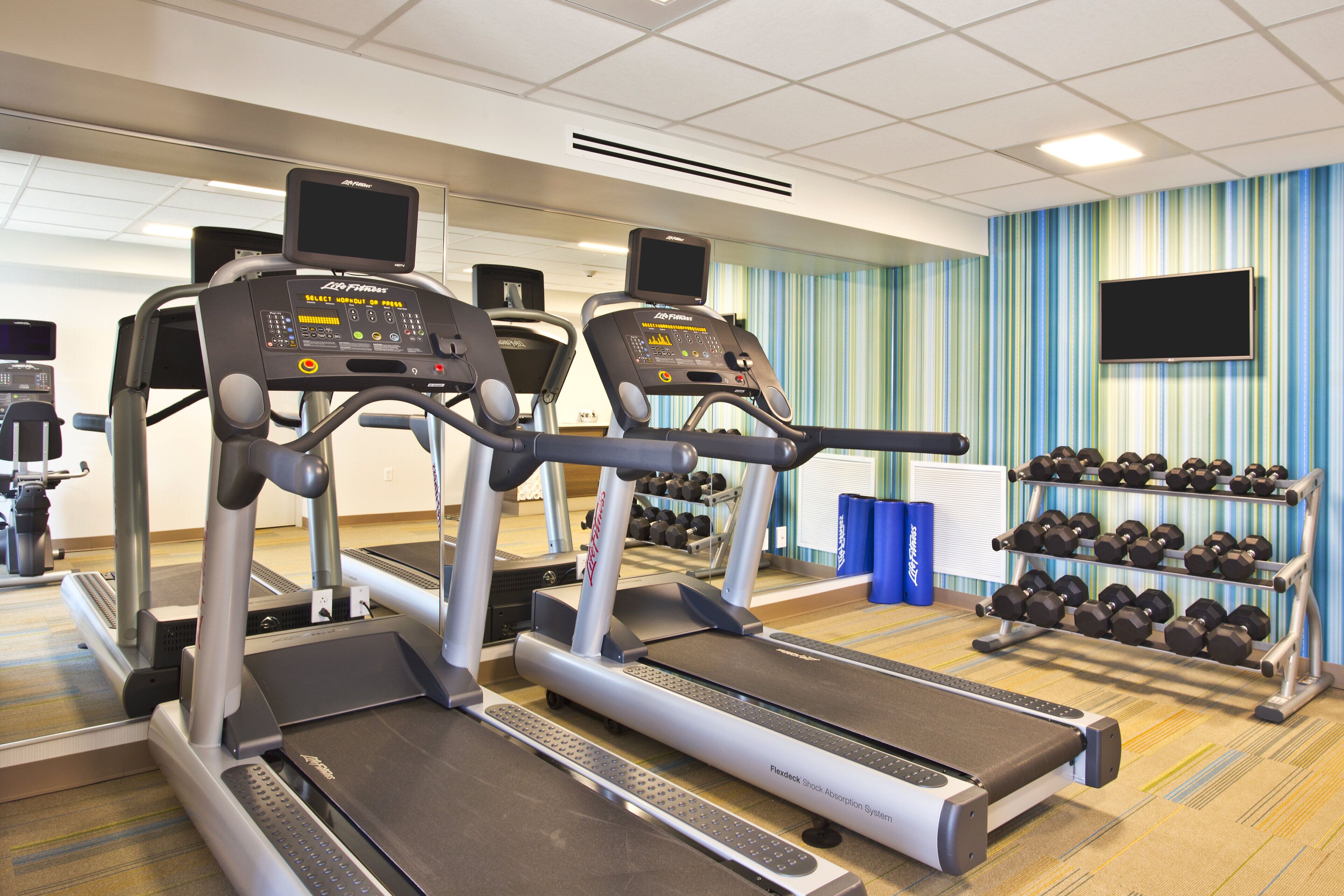 Ein Fitnessstudio mit Laufbändern, Kurzhanteln und einem Flexdeck Stoßabsorbationssystem.