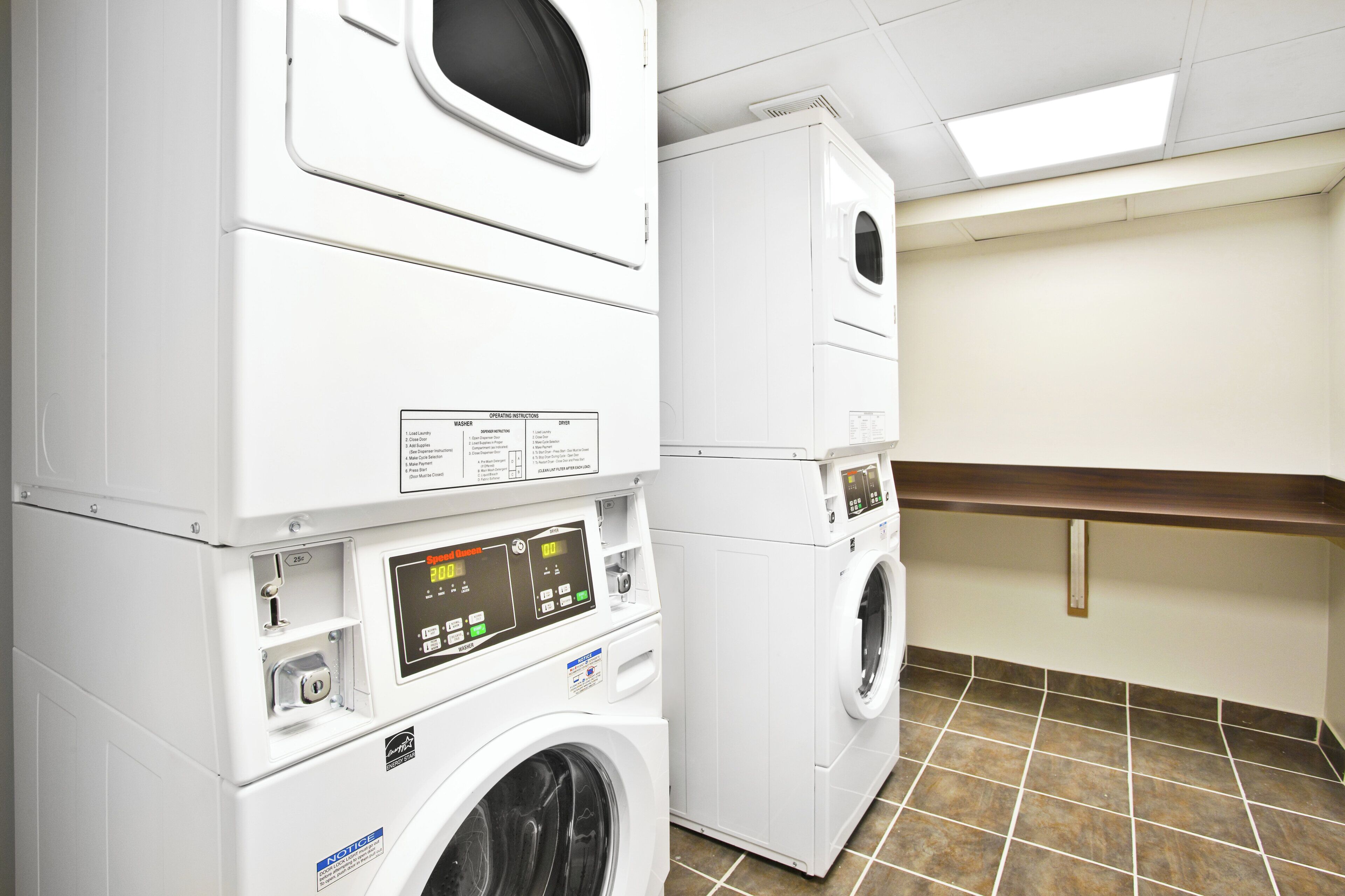 A laundry facility with stacked washers and dryers, control panels, and a tiled floor.