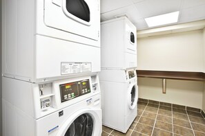 A laundry facility with stacked washers and dryers, control panels, and a tiled floor. - Holiday Inn Express Boston - Waltham by IHG (Waltham)