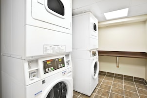 Un cuarto de lavandería con lavadoras y secadoras apiladas, paneles de control y piso de baldosas.