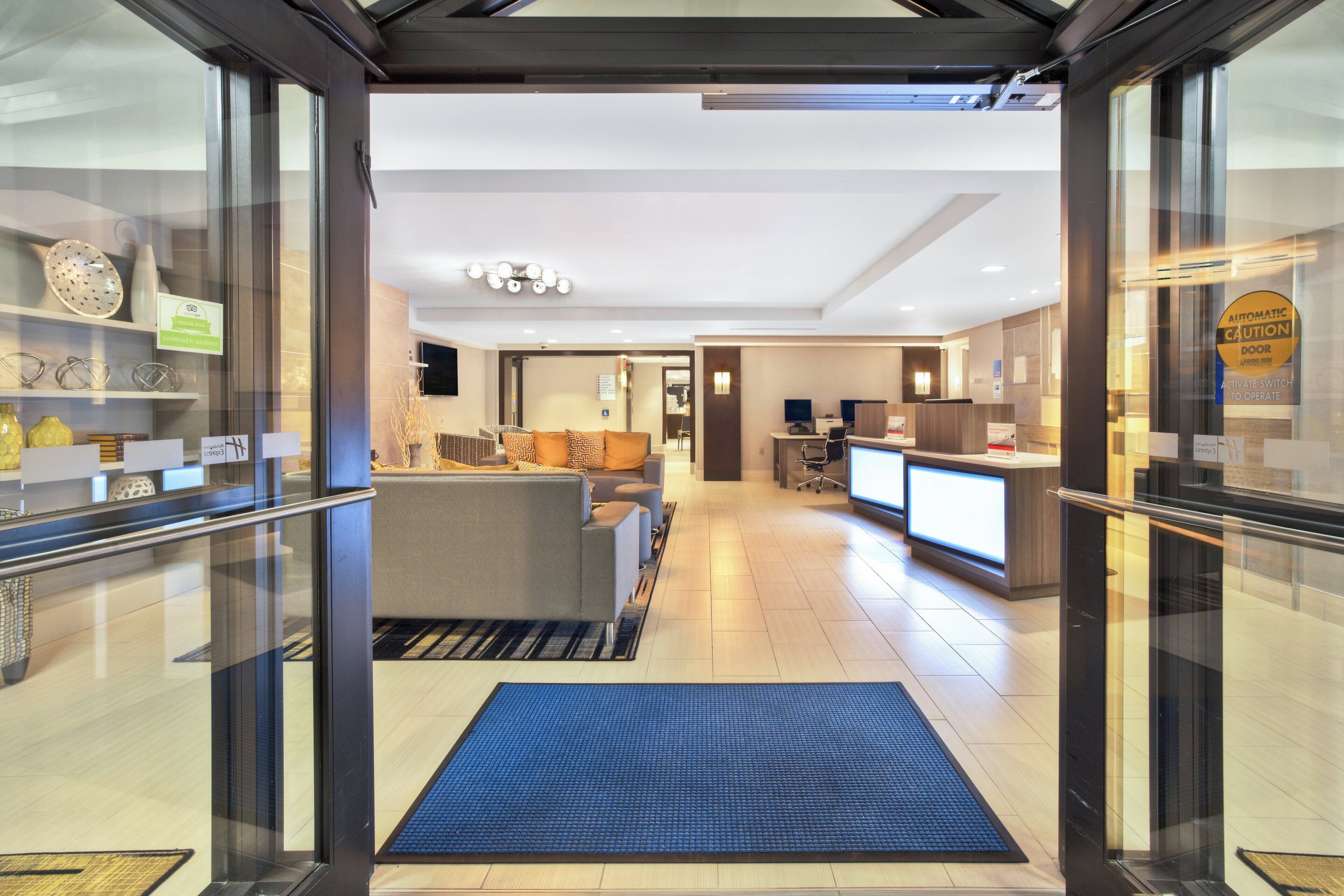 A hotel lobby with a reception desk, seating area, and a clear view of the interior through the glass doors.