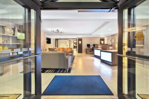 Un vestíbulo de hotel con mostrador de recepción, zona de estar y una vista despejada del interior a través de puertas de vidrio.