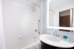 Un baño moderno con una bañera blanca, un espejo grande y un lavabo con artículos de aseo.