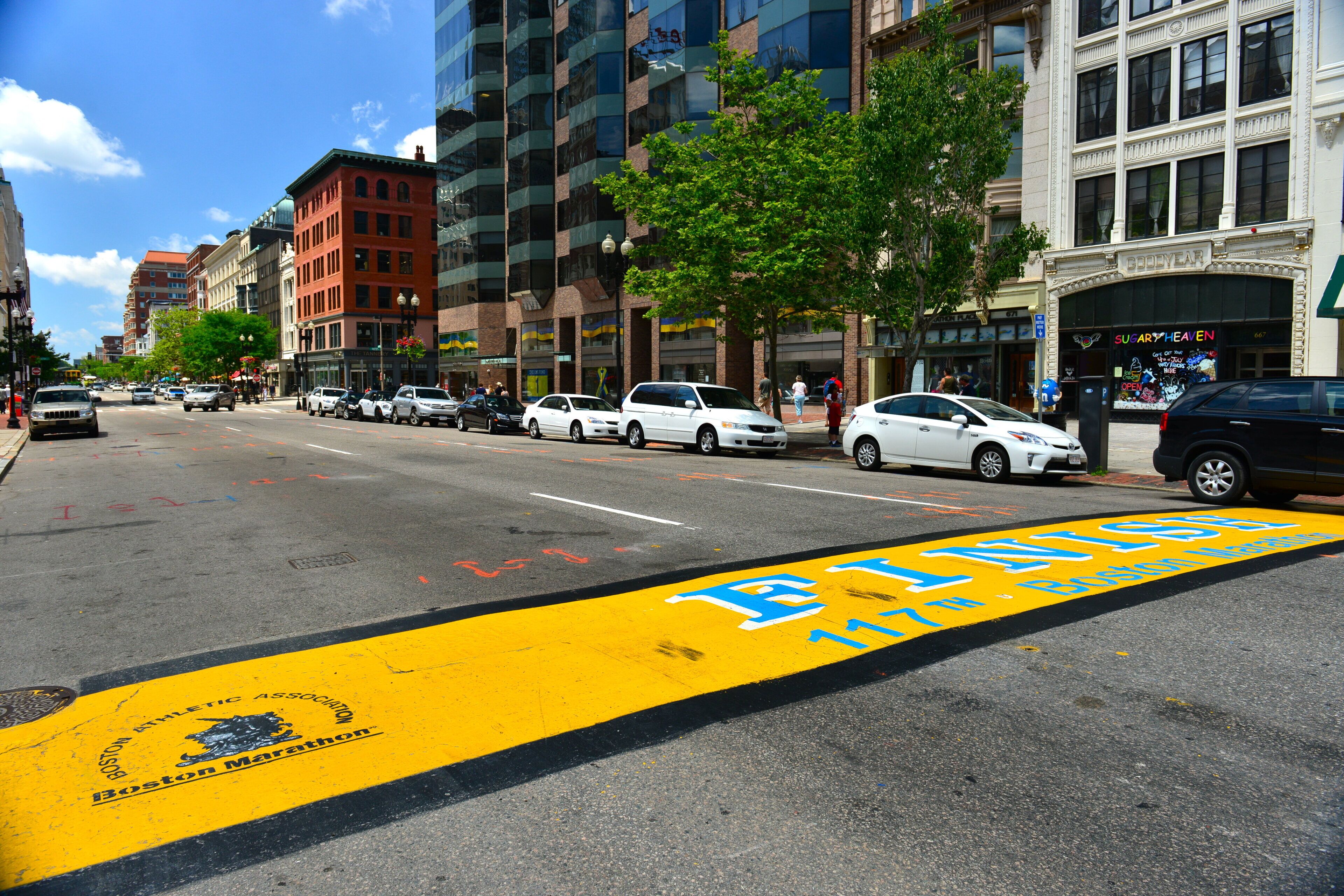 A street with a yellow bike lane, cars parked along the side, and buildings with various storefronts.