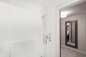 Un baño moderno con puerta de ducha de vidrio, espejo con marco de madera y una lámpara en la pared.