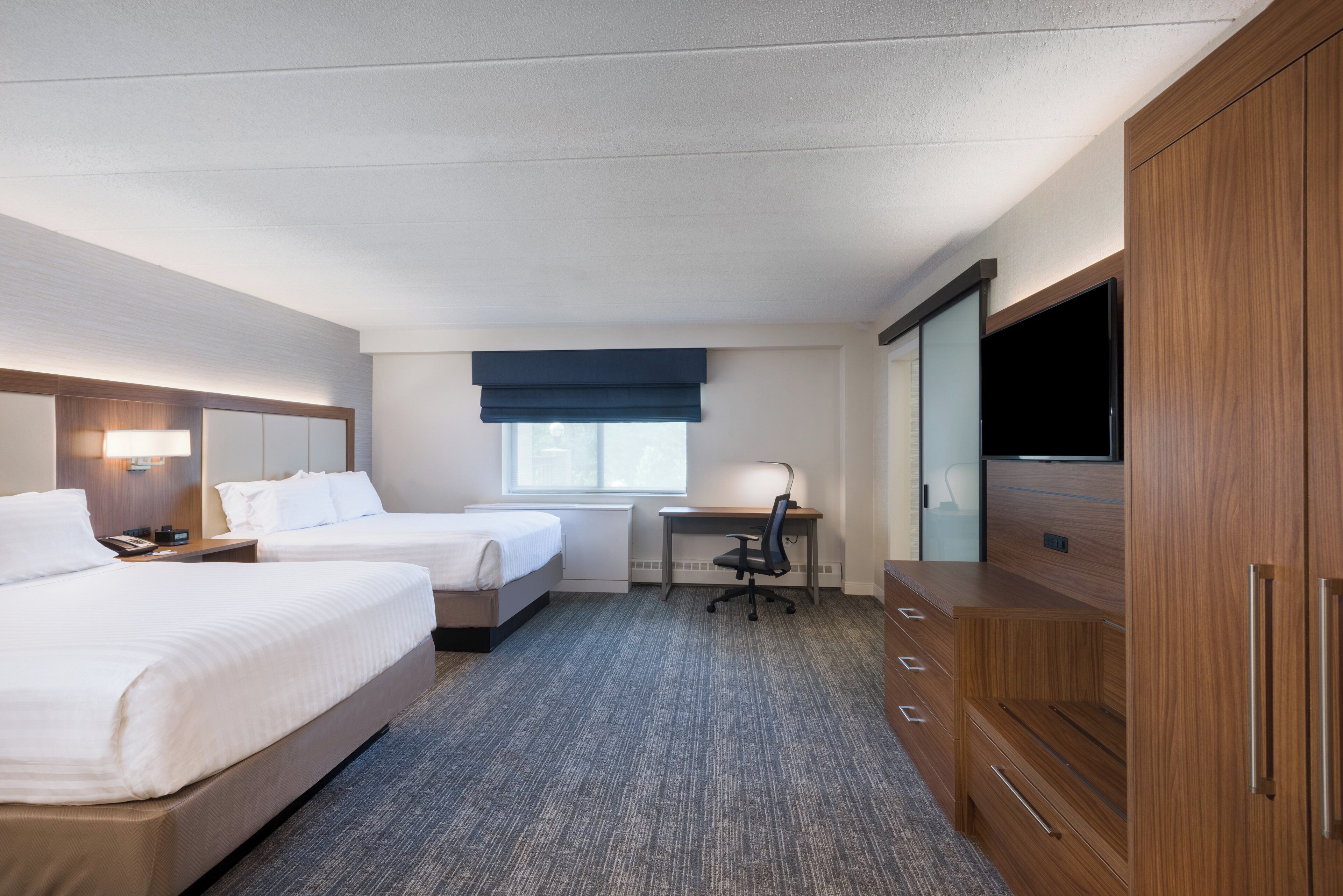 A hotel room with two beds, a desk, a chair, a TV, and a wardrobe.