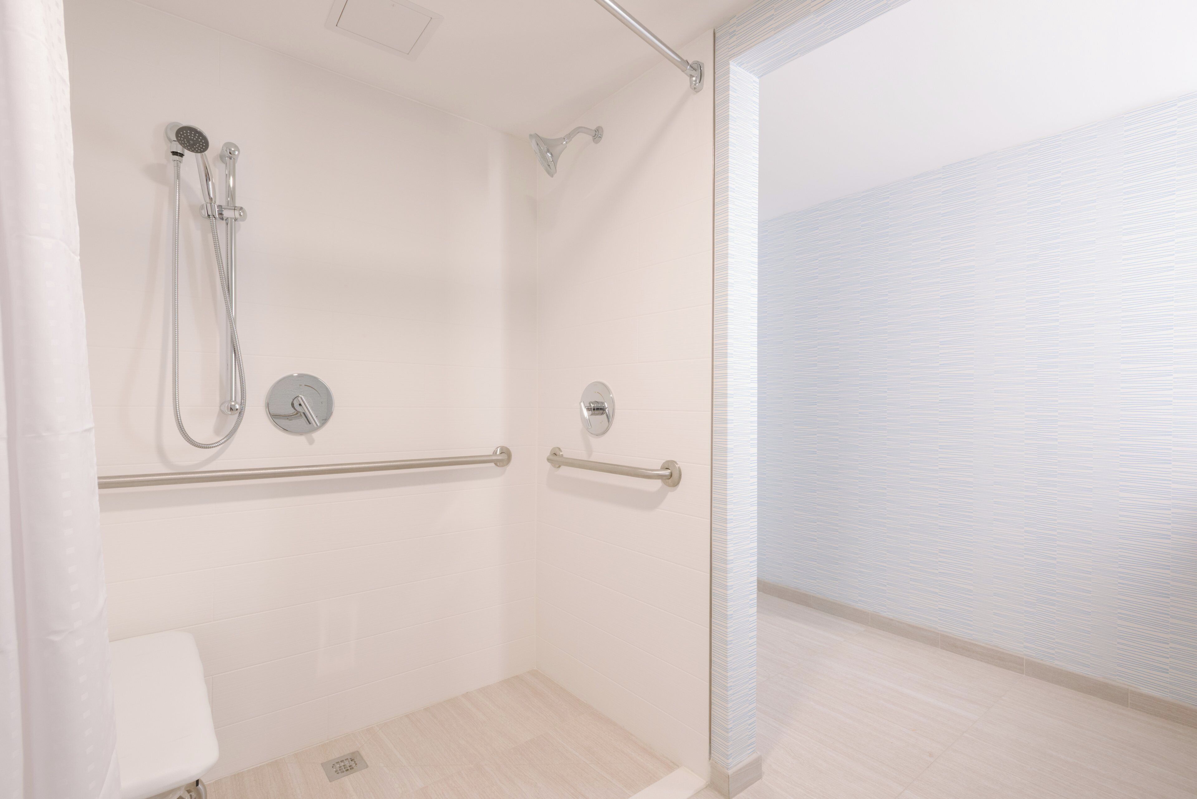 A shower area with a handrail, a control panel, and a tiled floor.