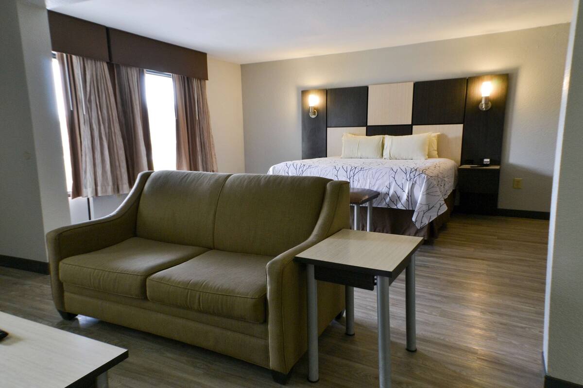 Ein Hotelzimmer mit Sofa, einem kleinen Tisch, einem Bett mit Kopfteil und einem Nachttisch.