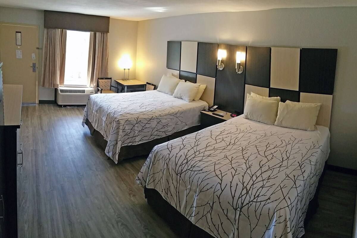 Ein Hotelzimmer mit zwei Betten, einem Schreibtisch, einem Stuhl und einem Fenster mit Vorhängen.