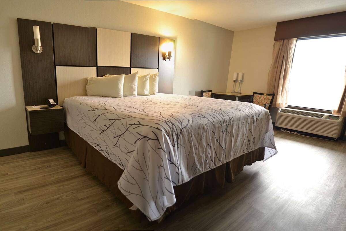 Ein Hotelzimmer mit einem großen Bett, einem Nachttisch, einer Wandlampe und einem Fenster mit Vorhängen.