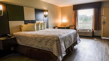 Una habitación de hotel con una cama grande, mesitas de noche, un escritorio, una silla, una ventana con cortinas y un equipo de aire acondicionado.