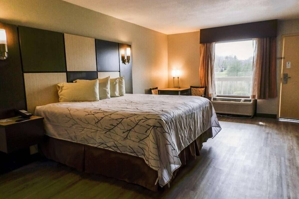 Ein Hotelzimmer mit einem großen Bett, Nachttischen, einem Schreibtisch und einem Fenster mit Vorhängen.