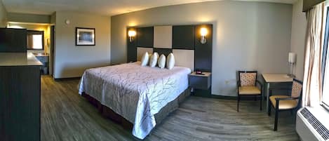 Een hotelkamer met een groot bed, nachtkastjes, een bureau met stoel en uitzicht op de gang.