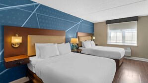 Une chambre d’hôtel avec deux lits, un mur bleu orné d’un motif géométrique, une fenêtre avec des stores et un plancher en bois.
