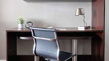 A modern office desk with a black office chair, a small potted plant, and a desk lamp.