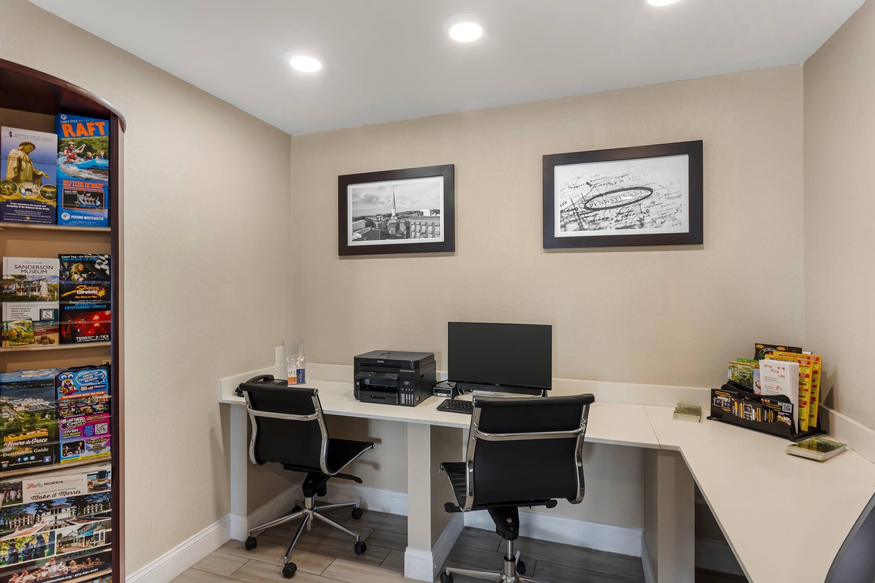 A modern office space with a desk, two chairs, a printer, and a bookshelf filled with travel guides.