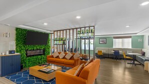 Un espace de détente moderne avec un mur végétal, des canapés orange, une table basse en bois et un téléviseur fixé au mur.