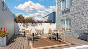 Une terrasse extérieure avec un plancher en bois, des murs blancs et un bâtiment en pierre en arrière-plan.