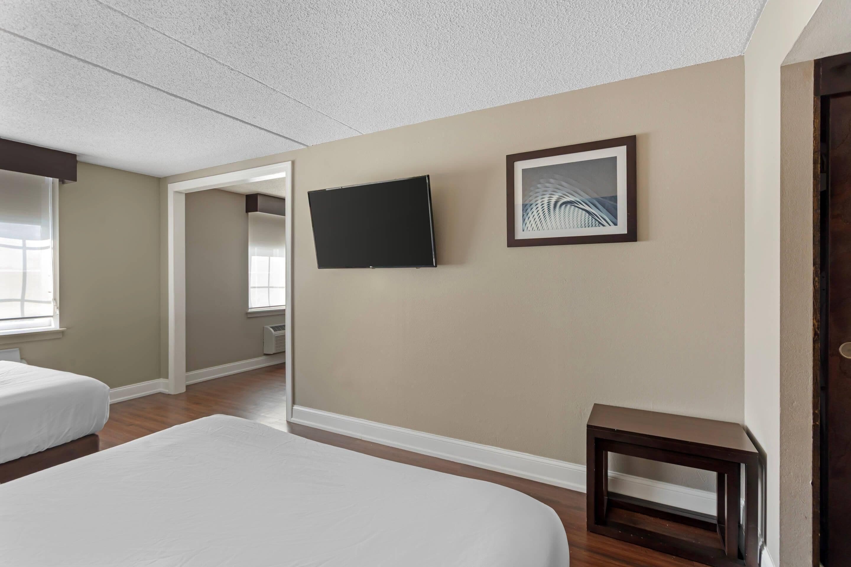 A hotel room with a large bed, a small bedside table, a flat-screen TV mounted on the wall, and a framed picture.