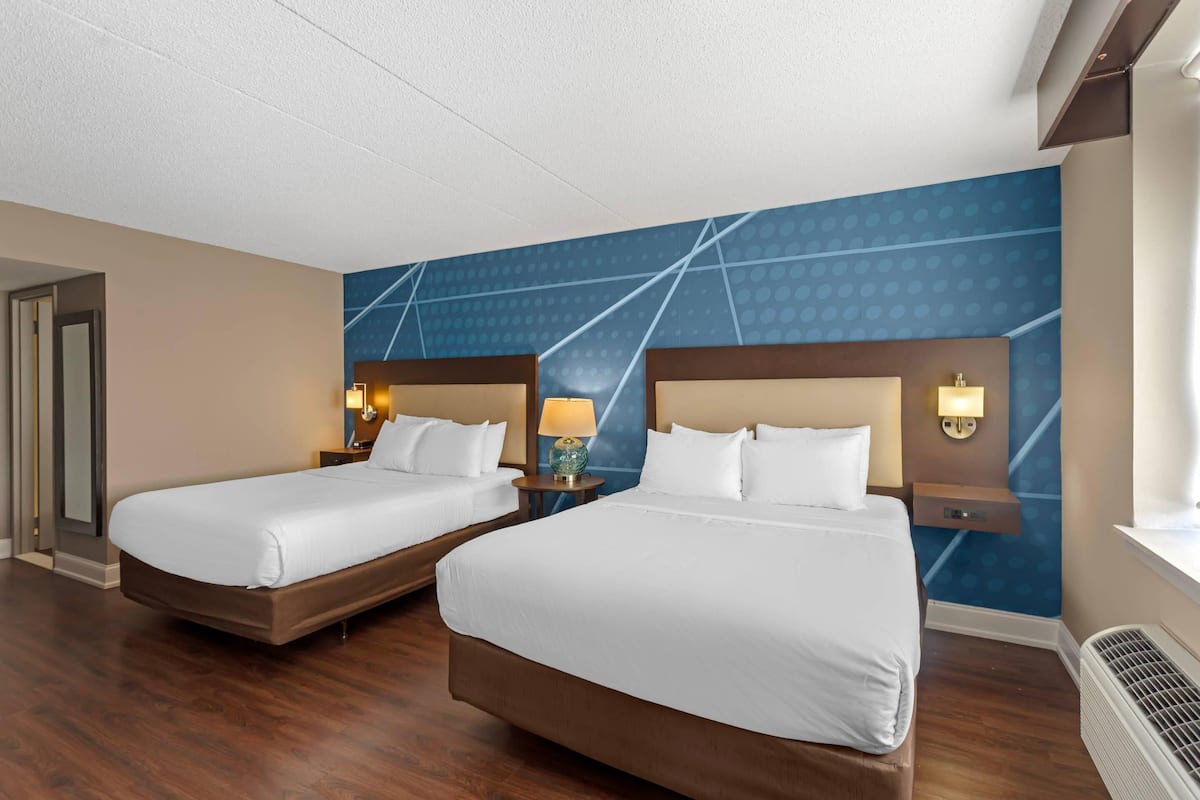 A hotel room with two beds, a blue patterned wall, and a wooden floor.