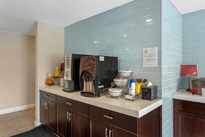 A hotel kitchenette with a coffee machine, a water dispenser, and a bowl of fruit.
