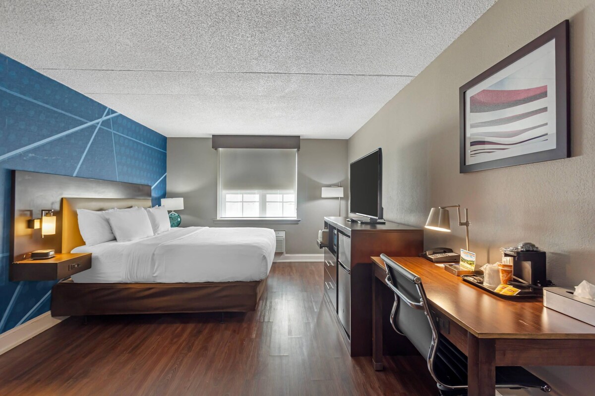 A hotel room with a bed, desk, and kitchenette.