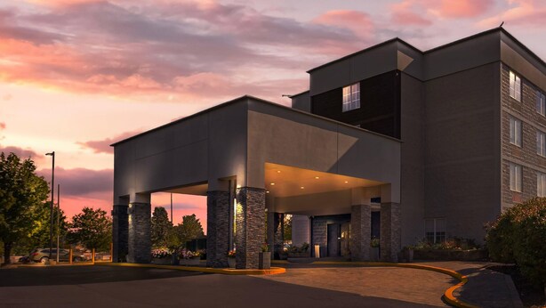 Un hôtel moderne doté d’une entrée couverte, de piliers en pierre et d’un parking.