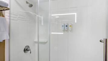 Cabina de ducha con paredes de vidrio, cabezal de ducha de mano, puerta de vidrio y un perchero con una toalla blanca.