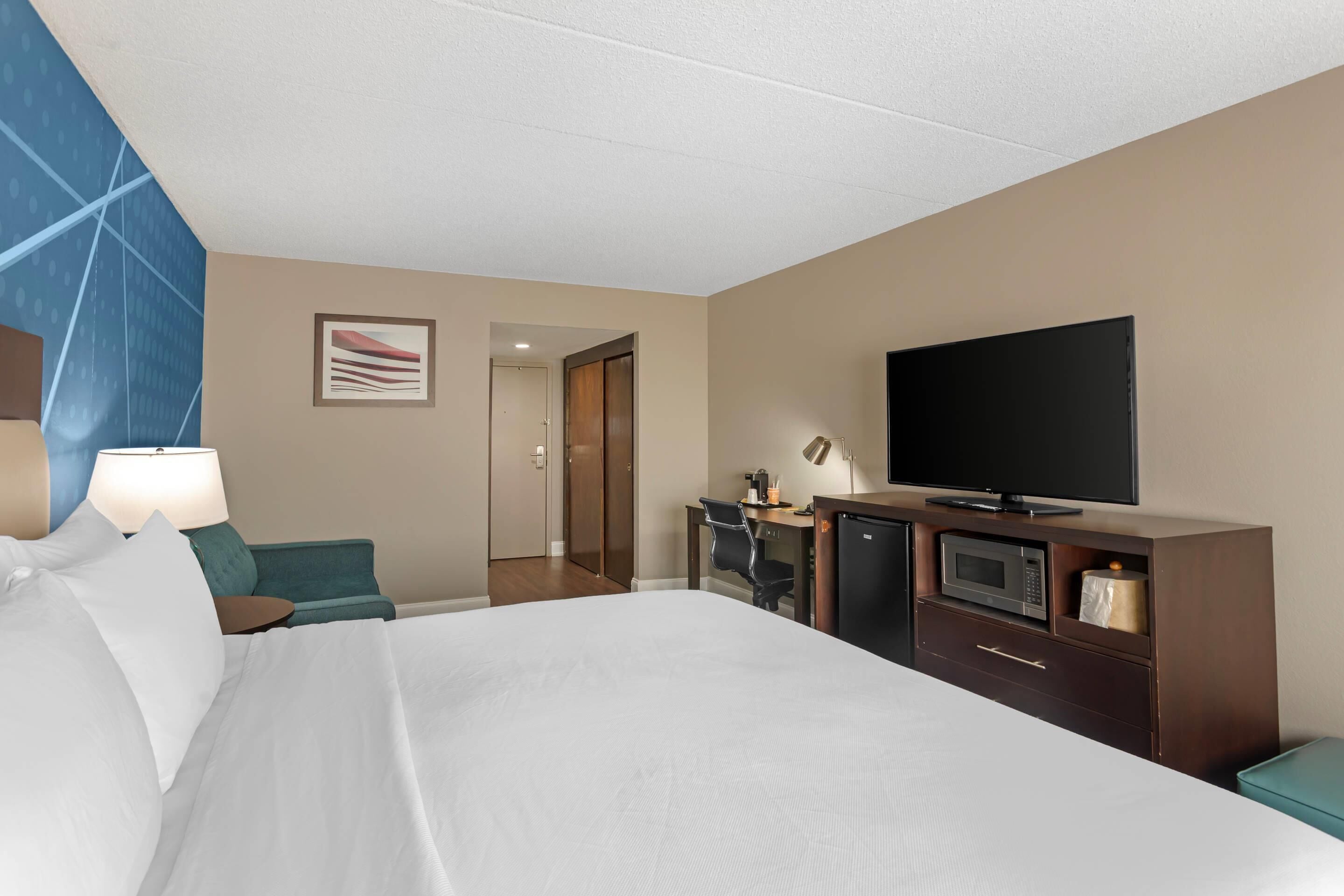 A hotel room with a bed, a desk with a computer, a television, and a microwave.