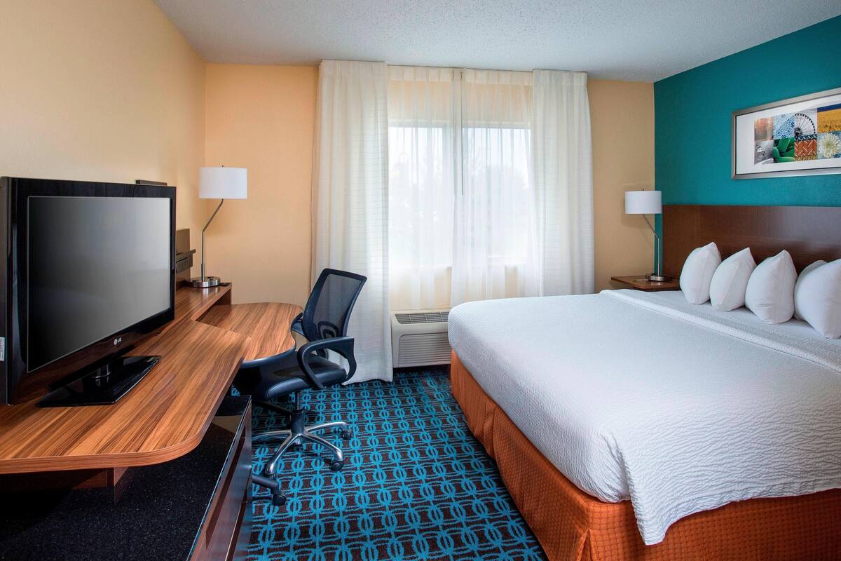 A hotel room with a bed, a TV, a desk, and a chair.