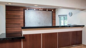 A reception area with a wooden panel wall, a black reception desk, a large window, and a clock on the wall. - Fairfield Inn & Suites by Marriott Branson (Branson)