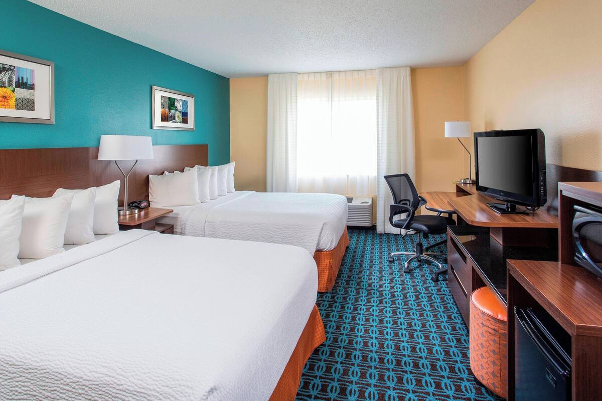 A hotel room with two beds, a desk with a computer, a television, and a bathroom.