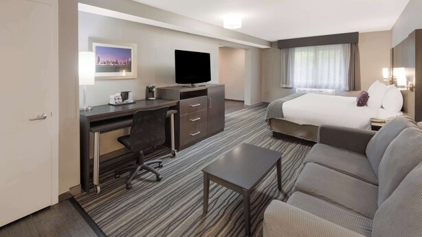 A hotel room with a bed, a sofa, a desk with a chair, a television, and a window with curtains.