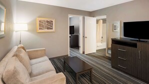 A hotel room with a sofa, a coffee table, a TV, and a cabinet. There is a door leading to a bathroom.