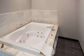 A modern bathroom with a marble-tiled wall, a white bathtub, and a dark wooden floor.