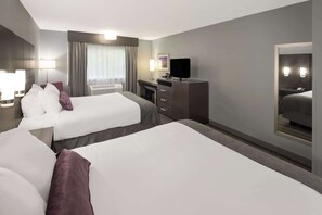 A hotel room with two beds, a desk, a TV, and a large mirror.