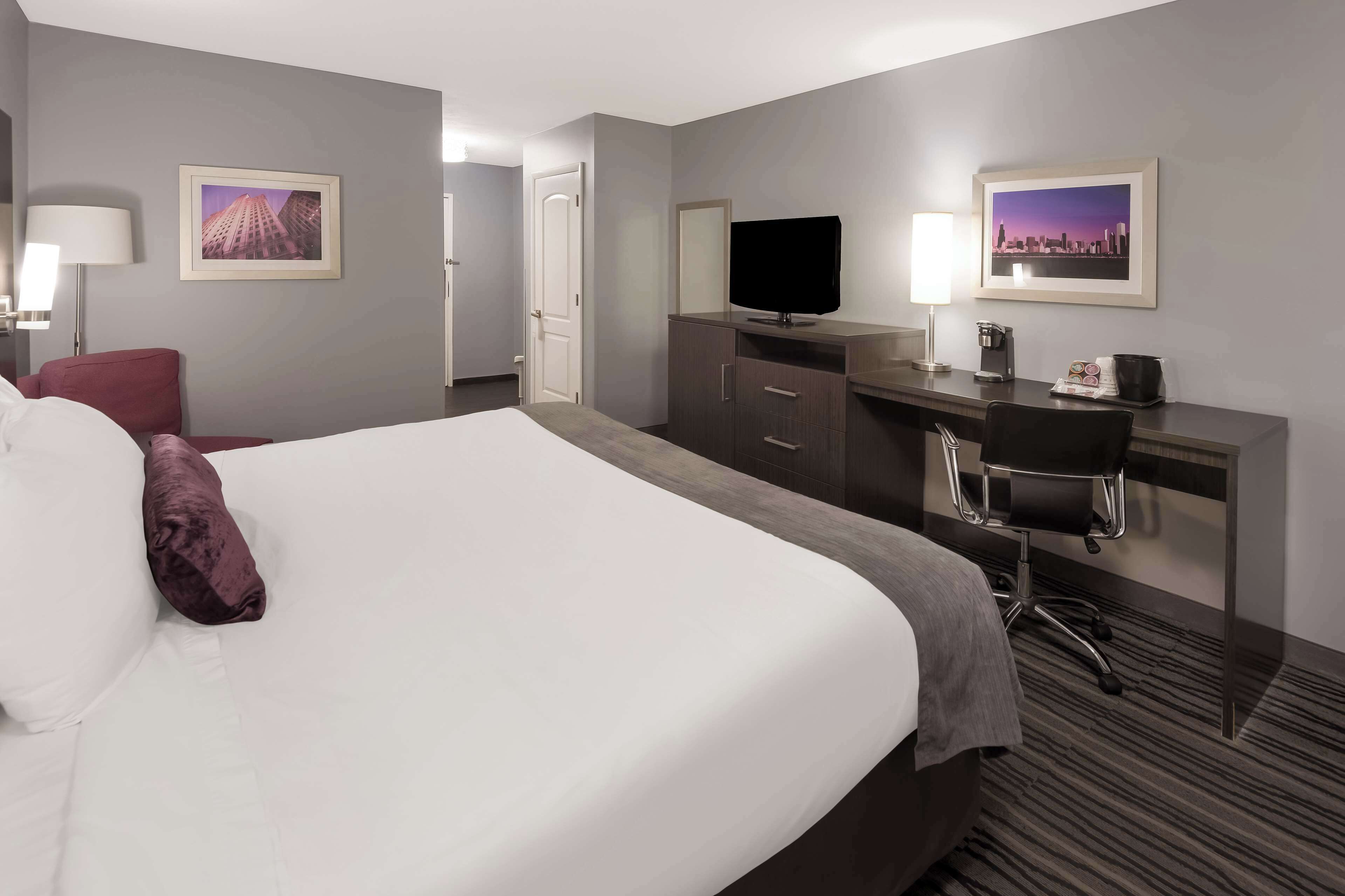 A hotel room with a large bed, a desk with a flat-screen TV, a chair, and two framed pictures on the walls.