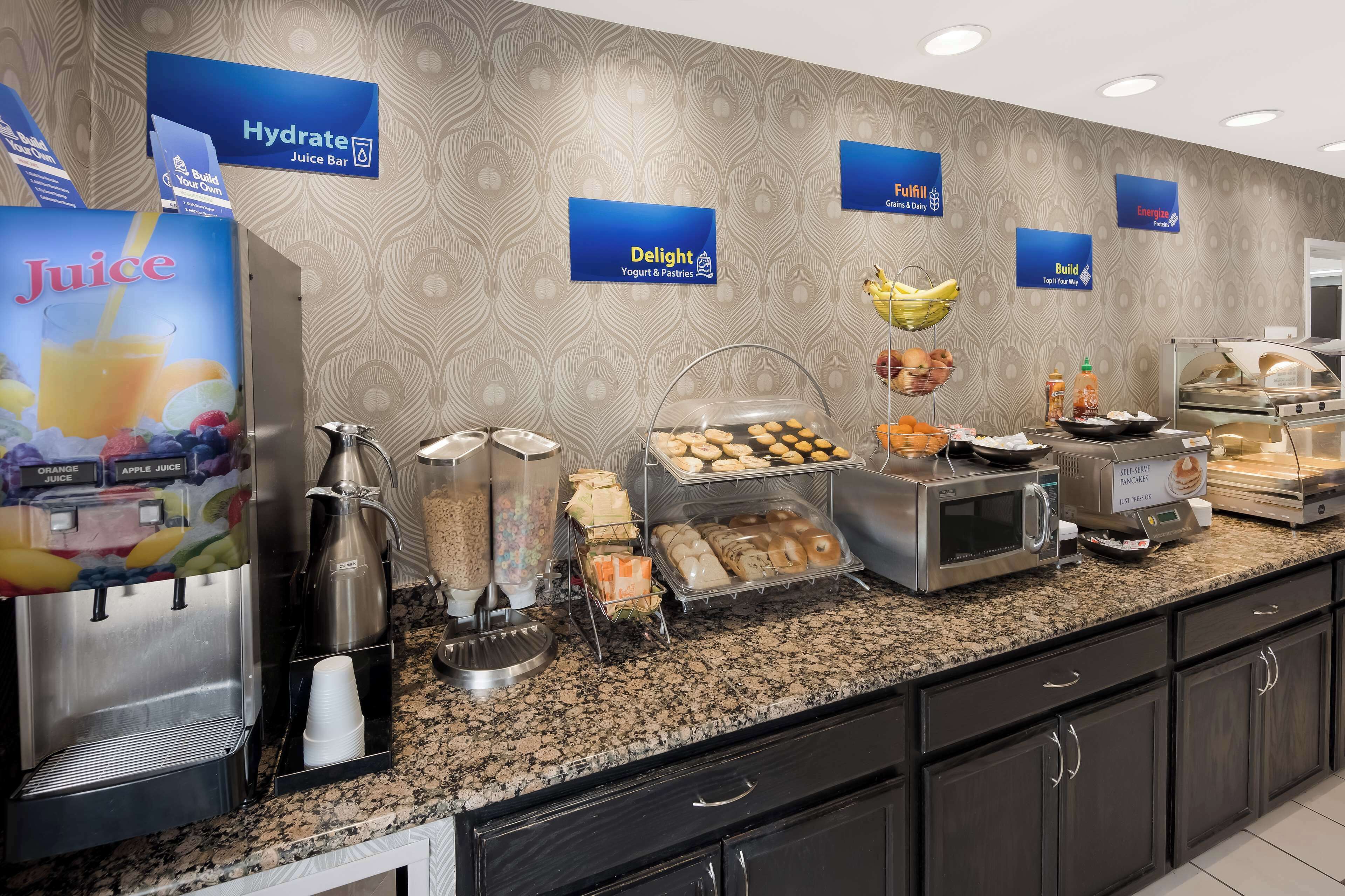 Een ontbijtbuffet met sapautomaten, yoghurt, gebak en een koffieapparaat.